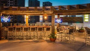 An outdoor bar area with a long counter, multiple chairs, and two televisions. - Fiesta Inn Puerto Vallarta Isla (Puerto Vallarta)