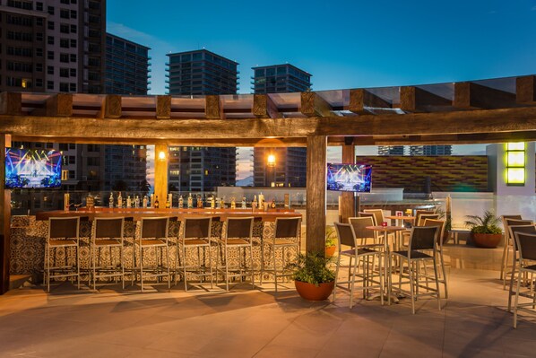 An outdoor bar area with a long counter, multiple chairs, and two televisions. - Fiesta Inn Puerto Vallarta Isla (Puerto Vallarta)