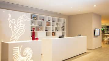A modern reception area with a white reception desk, a wall-mounted shelf with various items, and a digital display.