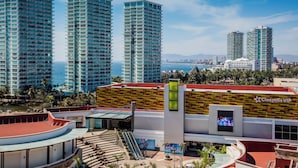 Een modern hotel met een gevel in rood en geel, een centraal atrium en uitzicht op de zee en omliggende wolkenkrabbers.