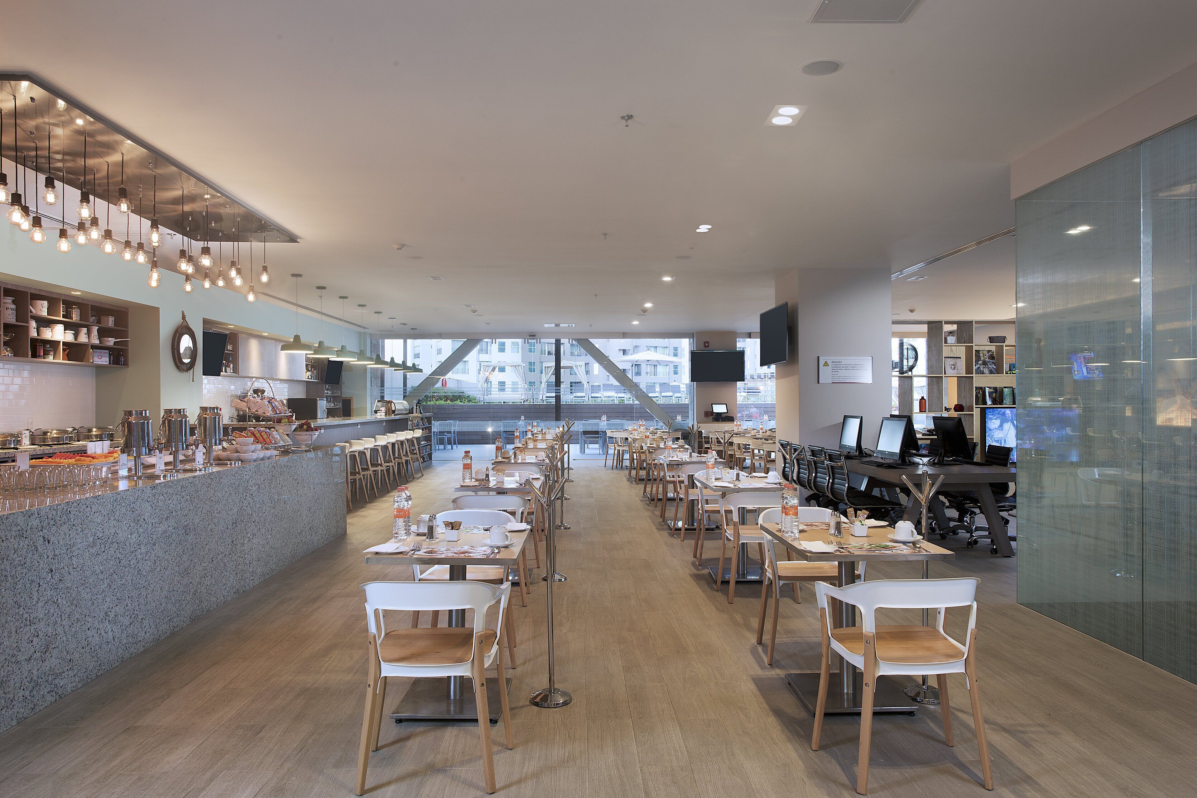 A modern restaurant with a long counter, multiple tables, and chairs.