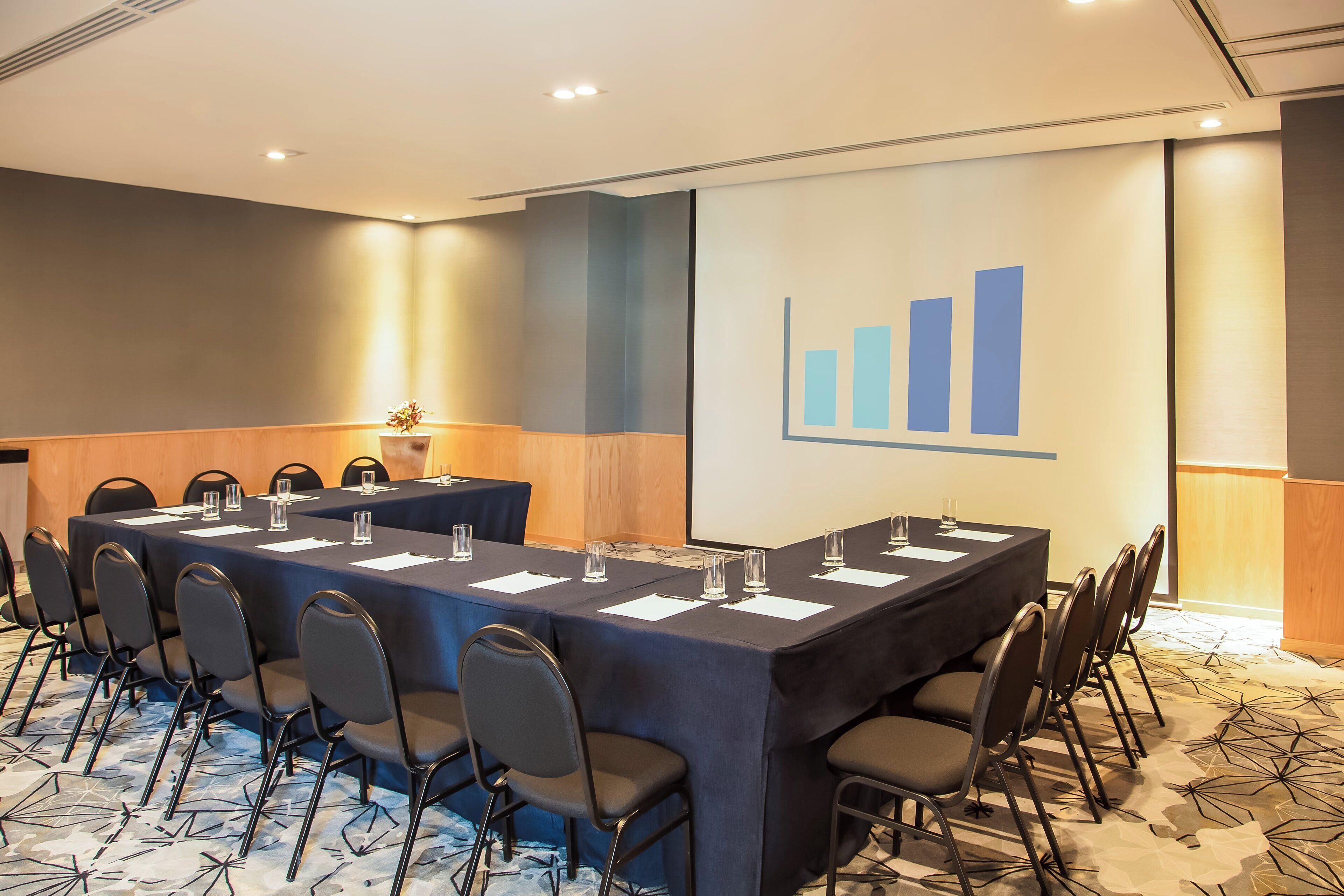 A conference room with a long table, chairs, and a presentation screen displaying a bar graph.