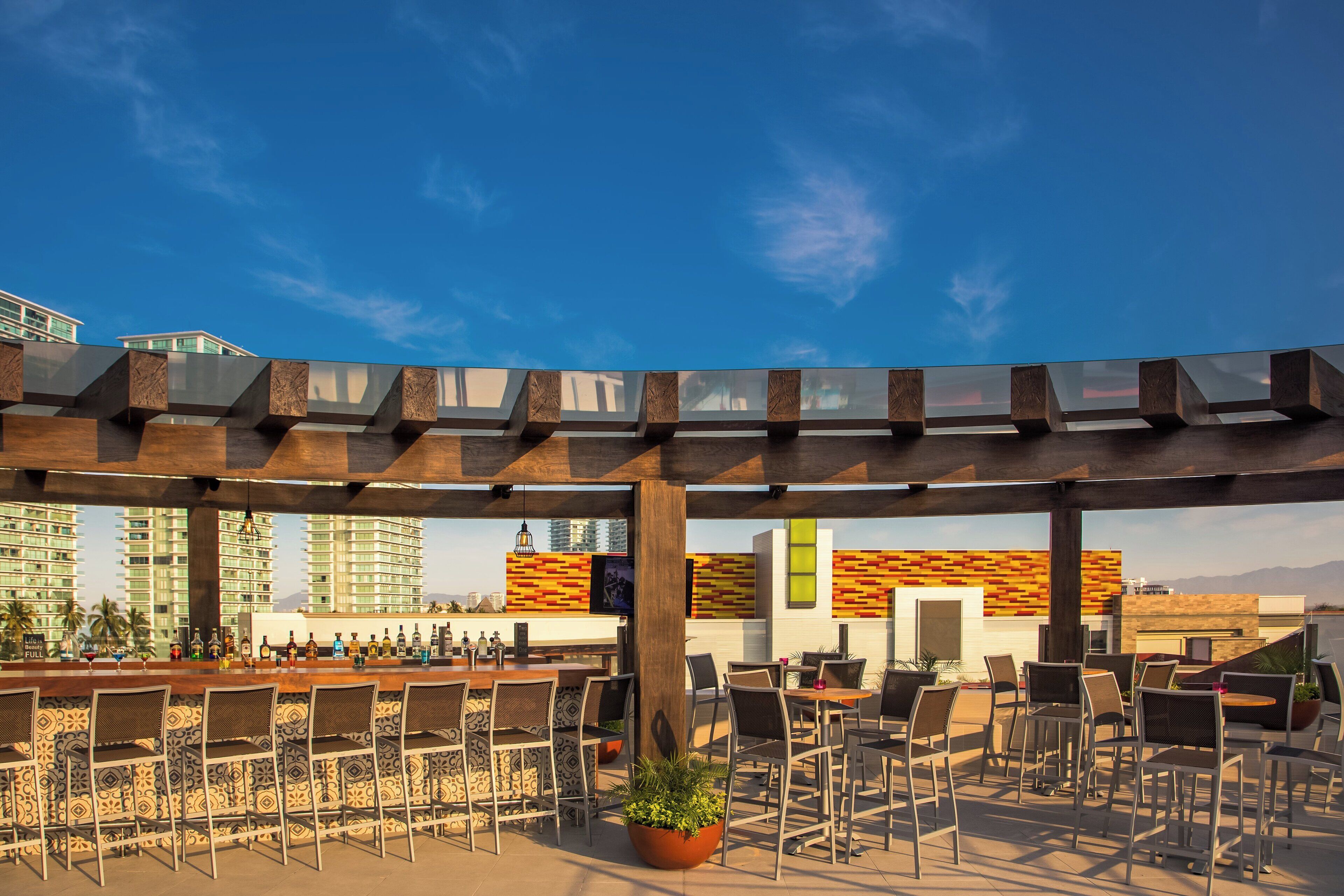 An outdoor bar area with a pergola, seating, and a view of buildings in the background.