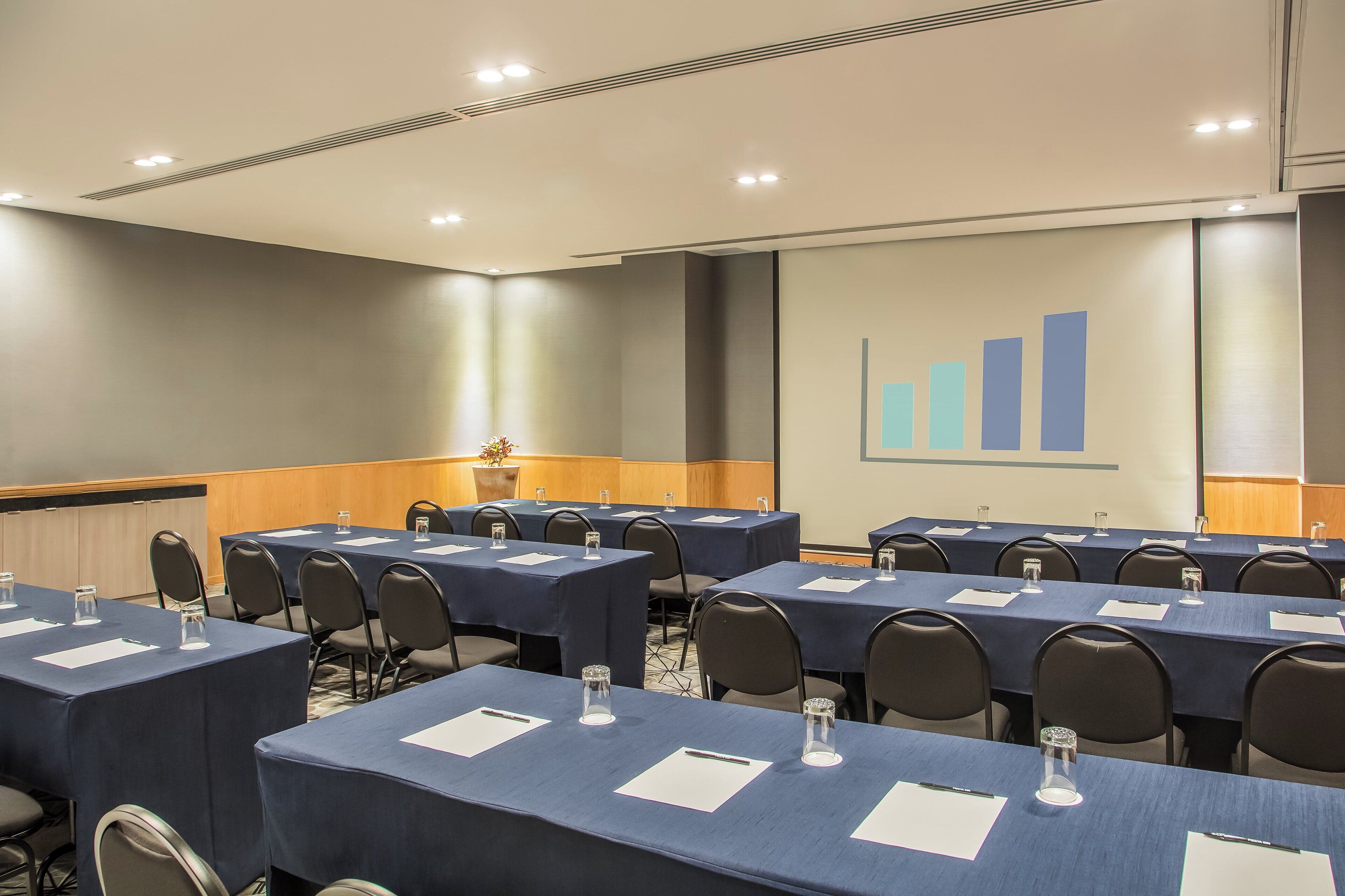 A conference room with multiple tables, chairs, and a presentation screen displaying a bar graph.