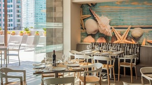 Een restaurant met terras, uitzicht op hoge gebouwen en een muurschildering van schelpen.
