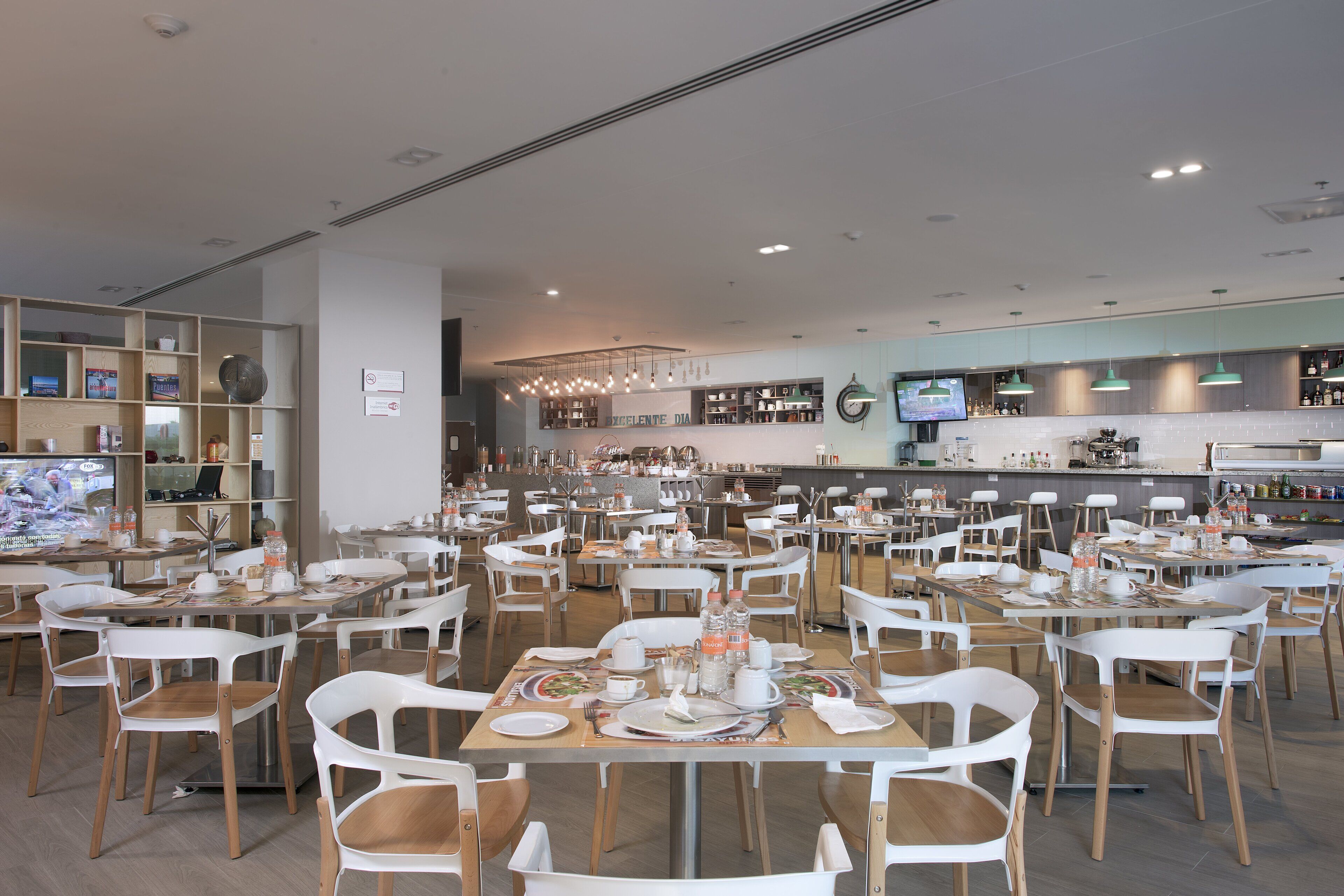 Un grand espace dédié à la salle à manger, avec plusieurs tables et chaises, une cuisine à l’arrière-plan et des étagères remplies de divers objets.