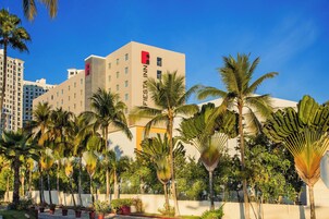 A hotel with a modern design, palm trees, and a clear blue sky.
