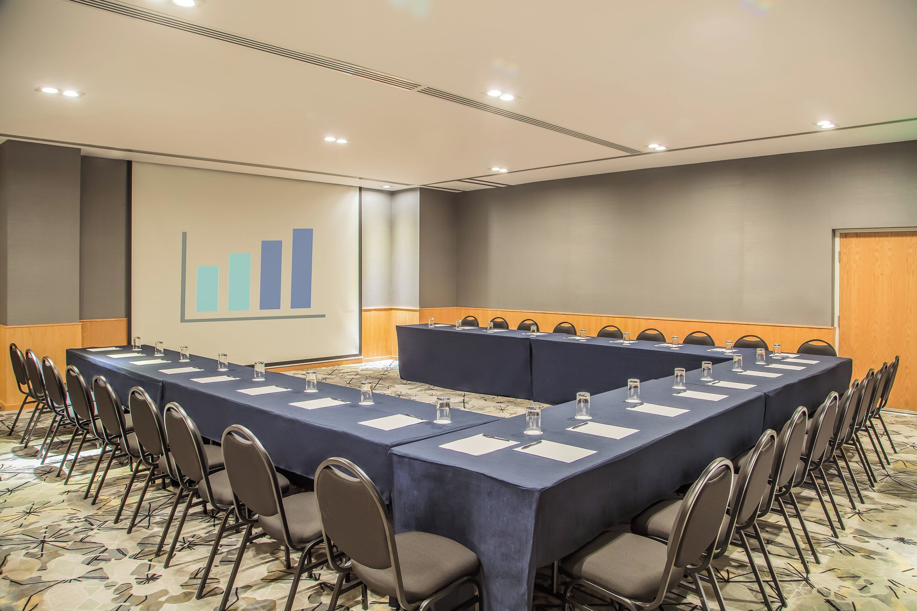 A conference room with a long table, chairs, and a presentation screen.