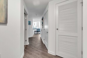 A hallway with white walls and wooden flooring leading to a dining area with a blue chair and a table. - Fully Furnished Apartments near Nationals Park (Washington)