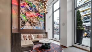 A modern lobby with a large abstract painting, a comfortable seating area, and a large window offering a view of the street. - Fully Furnished Apartments near Nationals Park (Washington)