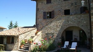A stone building with a staircase leading to an upper level, outdoor seating area, and potted plants. - Holiday Home in Montone with Pool & Garden (Montone)