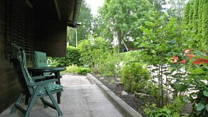 Un patio con tavolo e sedie, circondato da vegetazione rigogliosa e un giardino.