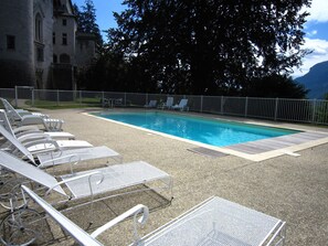 En swimmingpool med liggestole og en bygning af sten i baggrunden.