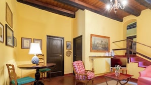 Een gezellige woonkamer met een houten plafond, een ronde tafel met een lamp, een stoel met een kussen, een roze bank en een trap.