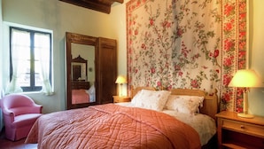 Een slaapkamer met een groot bed, een houten garderobe, een spiegel en bloemenbehang.