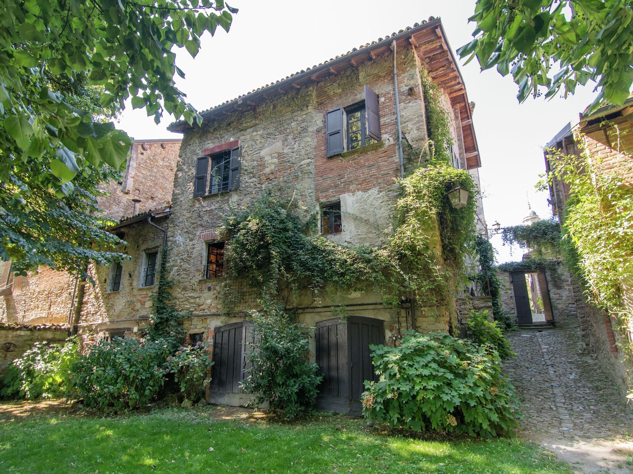 A rustic stone building with ivy-covered walls, a wooden door, and a small garden area.