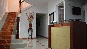 Un hall d’hôtel avec un escalier en marbre, un comptoir d’accueil et un téléviseur fixé au mur.