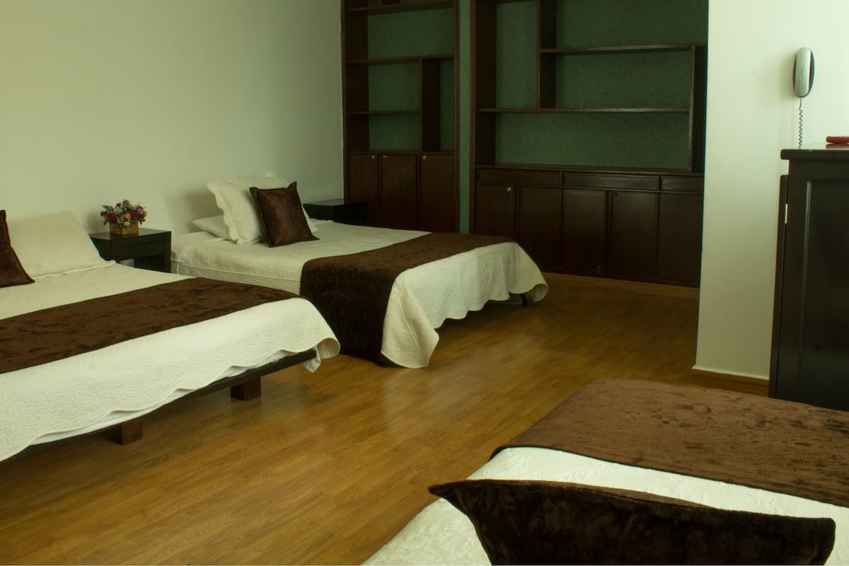 Ein Hotelzimmer mit zwei Einzelbetten, einem Holztisch, einem Telefon und einem Fenster mit grünem Rahmen.