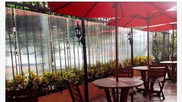 Un espace extérieur aménagé en terrasse, avec des tables et des chaises en bois rondes, des parasols rouges et des plantes en pot.