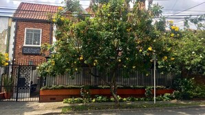 Un hôtel à la façade en briques, doté d’une entrée fermée par un portail et orné d’un arbre aux fleurs jaunes devant l’entrée.