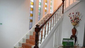 Un escalier avec des marches en marbre et une rampe en bois, menant à un palier doté d’une balustrade en verre et d’un vase rempli de fleurs.