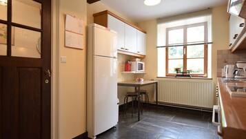 Een kleine keuken met een koelkast, magnetron en een raam met jaloezieën.