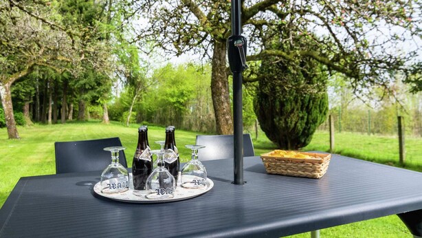 An outdoor table with a black umbrella, a tray with wine bottles and glasses, and a basket of bread.