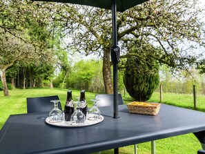 An outdoor table with a black umbrella, a tray with wine bottles and glasses, and a basket of bread.