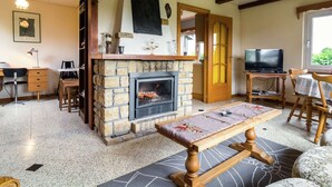 A cozy living room with a stone fireplace, wooden beams, a dining table, and a television.