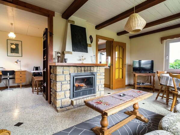 A cozy living room with a stone fireplace, wooden beams, a dining table, and a television.