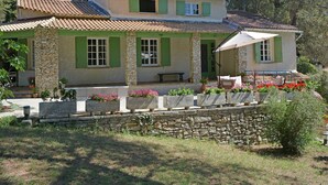 Une maison à deux étages, avec une façade en pierre, des volets verts et un toit recouvert de tuiles.