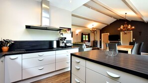 A modern kitchen with white cabinetry, a black countertop, and a built-in stove. There is a dining area with a wooden table and chairs, and a chandelier hanging above. - Luxurious Chalet in Beauraing with Sauna (Beauraing)