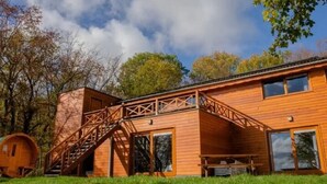 A wooden cabin with a staircase leading to a deck, surrounded by trees. - Luxurious Chalet in Beauraing with Sauna (Beauraing)