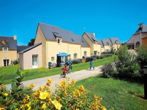 A residential area with houses, a pathway, and yellow flowering plants. - Brittany Retreat w/ Pool (Le Tronchet)