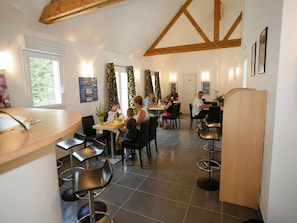 A restaurant with multiple tables and chairs, a wooden ceiling, and a tiled floor. - Brittany Retreat w/ Pool (Le Tronchet)