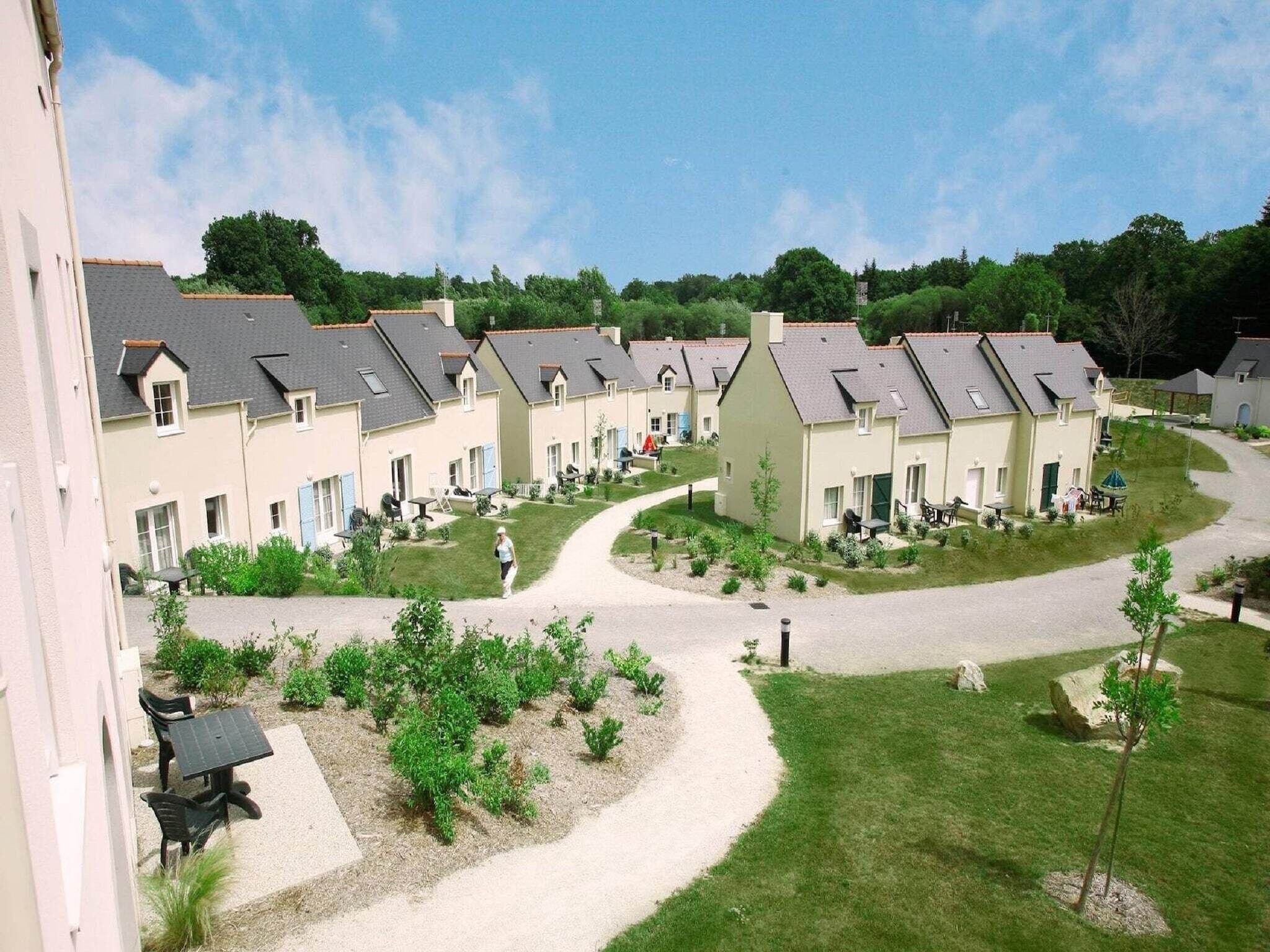 Eine Reihe von Wohnhäusern mit einem zentralen Innenhof, umgeben von Grünflächen und blauem Himmel.