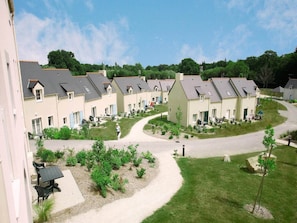 A row of residential buildings with a central courtyard, surrounded by greenery and a clear sky. - Brittany Retreat w/ Pool (Le Tronchet)