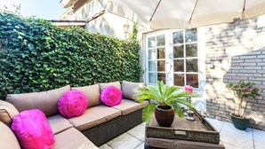 Un espace extérieur aménagé avec un banc rembourré, une plante en pot et un plateau en osier.