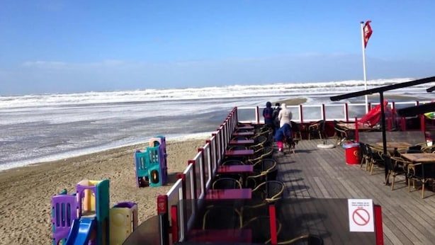 Un restaurant situé en bord de mer, avec une terrasse, une vue sur l’océan et un drapeau.