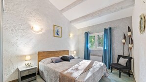 Quarto com cama, mesas de cabeceira, uma cadeira e janela com cortinas.