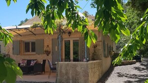 Uma casa rústica com parede de pedra, um pátio com móveis de exterior e uma entrada com estacionamento em cascalho.