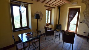 A rustic room with a wooden ceiling, a table with chairs, a lamp, a stove, and a window with a view of greenery. - Countryside cottage in Pergola (Pergola)