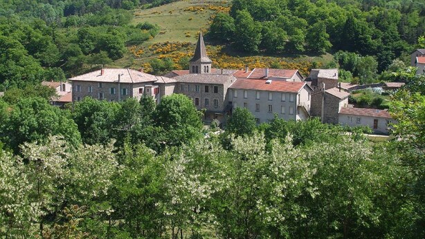 A cluster of stone buildings with a prominent church steeple, surrounded by lush greenery and hills in the background. - Rustic Retreat in Goutte-Claire (Sauvain)