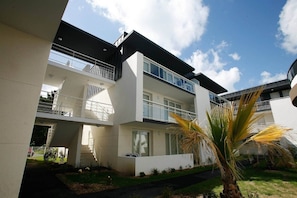 A modern multi-story residential building with balconies, large windows, and a well-maintained garden.