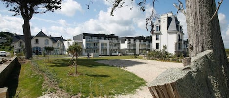 A residential area with modern and traditional buildings, a sandy path, and a large tree.