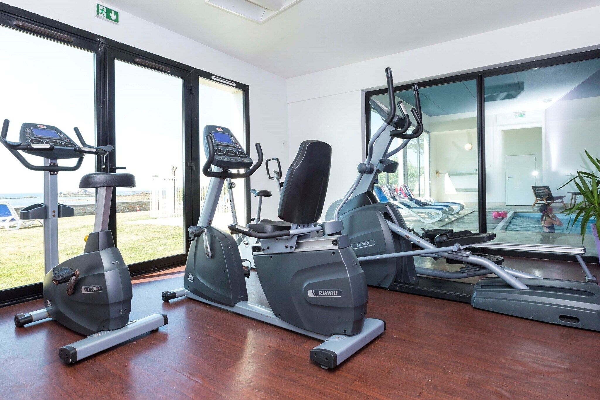 A gym with cardio machines, a pool, and a view of the outdoors.