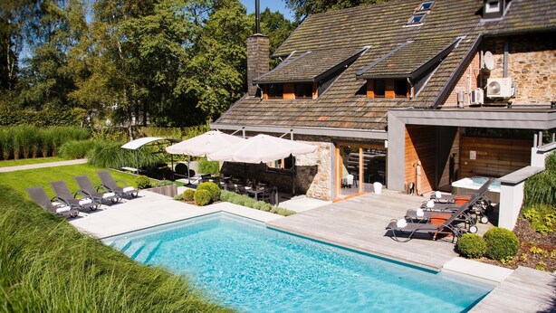 Ein modernes Haus mit Swimmingpool, Sitzgelegenheiten im Freien und einer Steinfassade.