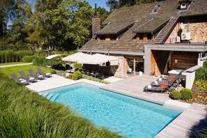 Ein modernes Haus mit Swimmingpool, Sitzgelegenheiten im Freien und einer Steinfassade.