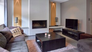 Ein modernes Wohnzimmer mit Sofa, Couchtisch, Fernseher, Kamin und Pendelleuchten.