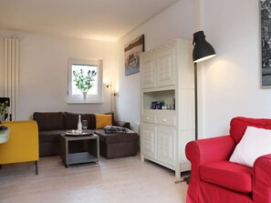 Ein Wohnzimmer mit einer Couch, einem roten Sitzsofa, einem Schrank, einer Stehlampe und einem Fenster mit einer Pflanze.